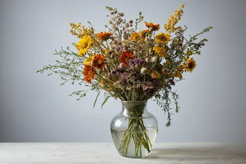 A glass vase with dried flowers on a white wooden table