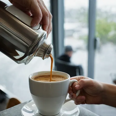 A person pouring espresso into a white cup while holding the handle