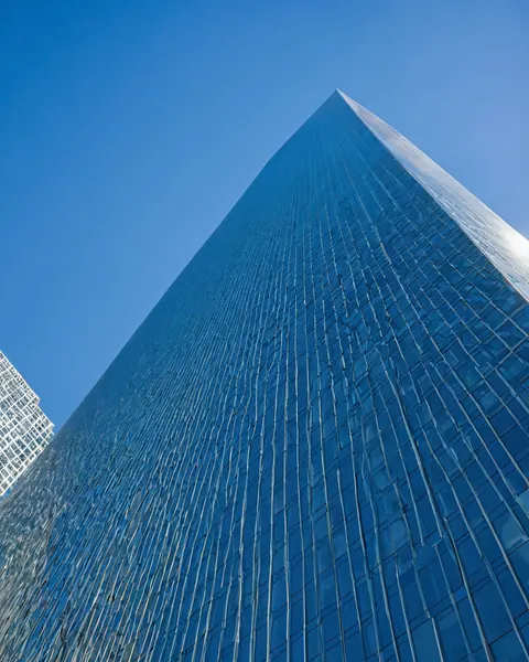 A tall glass skyscraper with a pointed top rises against a clear blue sky.