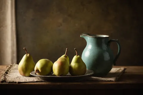 Four pears and a teal pitcher on a wooden table with burlap cloth.
