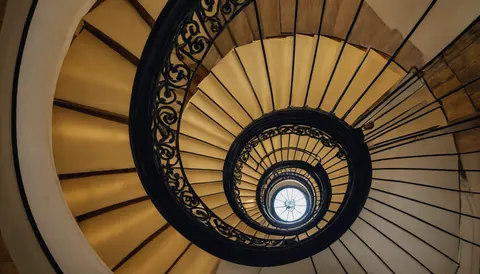 Spiral staircase with black iron railings and wooden steps leading upward to a skylight.