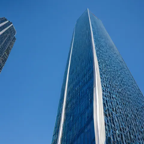 Towering glass skyscraper with blue panels and white stripes against clear blue sky