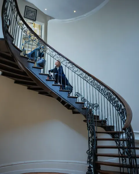 Woman in blue suit sitting on ornate wooden staircase looking up